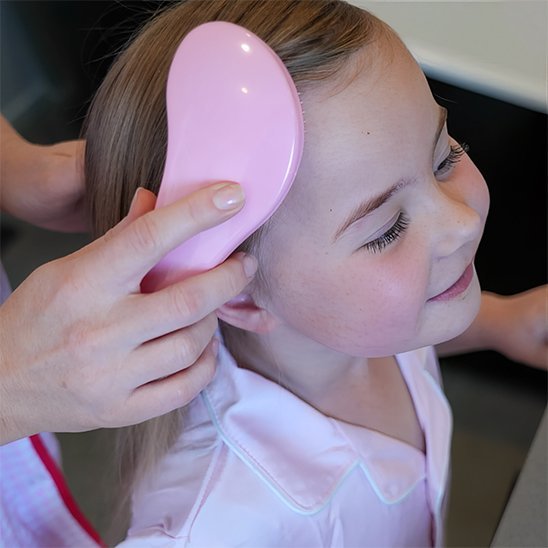 Brosse à cheveux Jeune femme souriante utilisant le peigne de massage crânien rose poudré pour stimuler son cuir chevelu