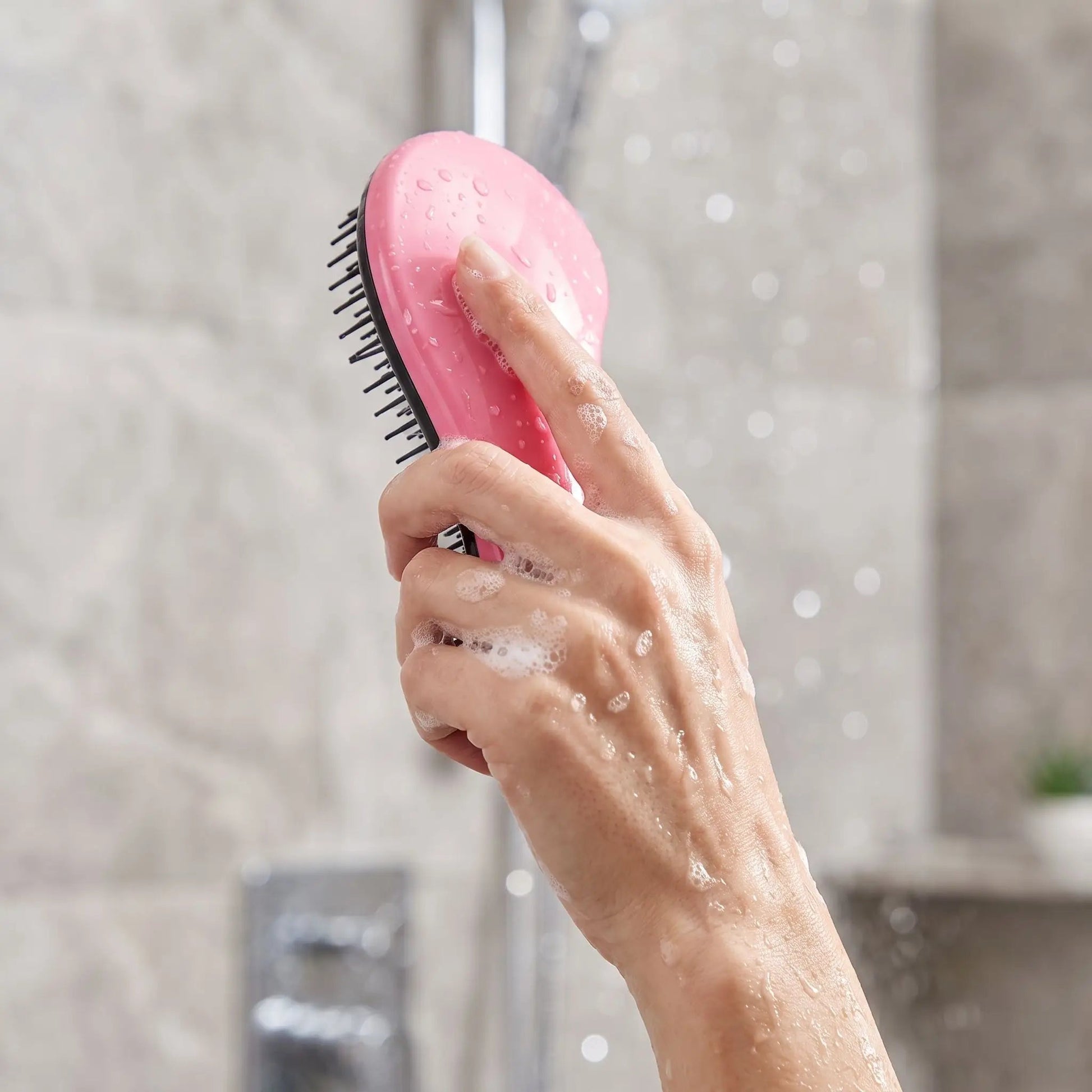 Brosse-a-cheveux-en-Gros-plan_-d_une-main-tenant-la-brosse-rose-poudre-ergonomique-sous-la-douche-avec-de-la-mousse.